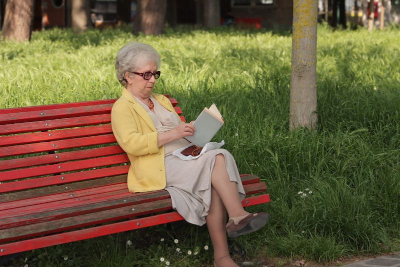 Donna anziana sorridente che legge all'aperto in un giardino italiano
